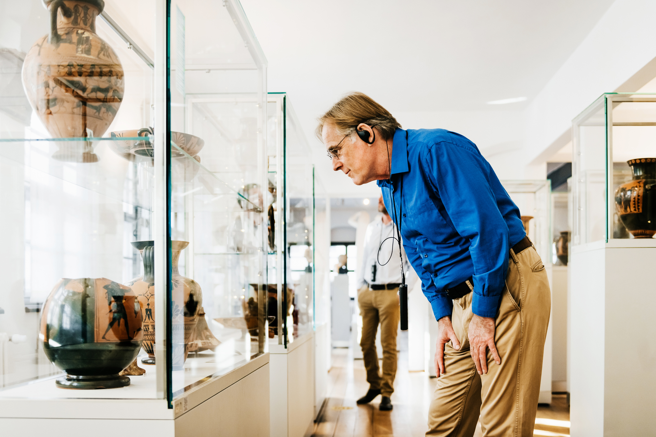 Homme mature visitant un musée d'antiquités. Il regarde un vase ancien avec attention et porte un casque audio.