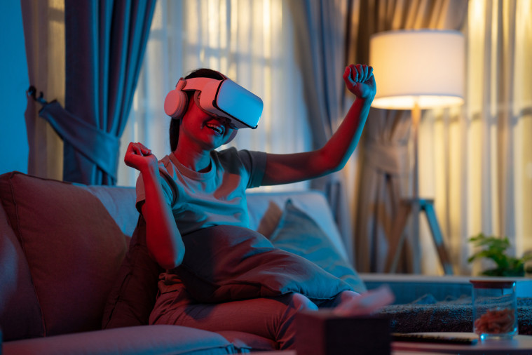 Jeune femme portant un casque de réalité virtuelle, un casque audio, et dansant dans son salon en vivant un concert en VR.
